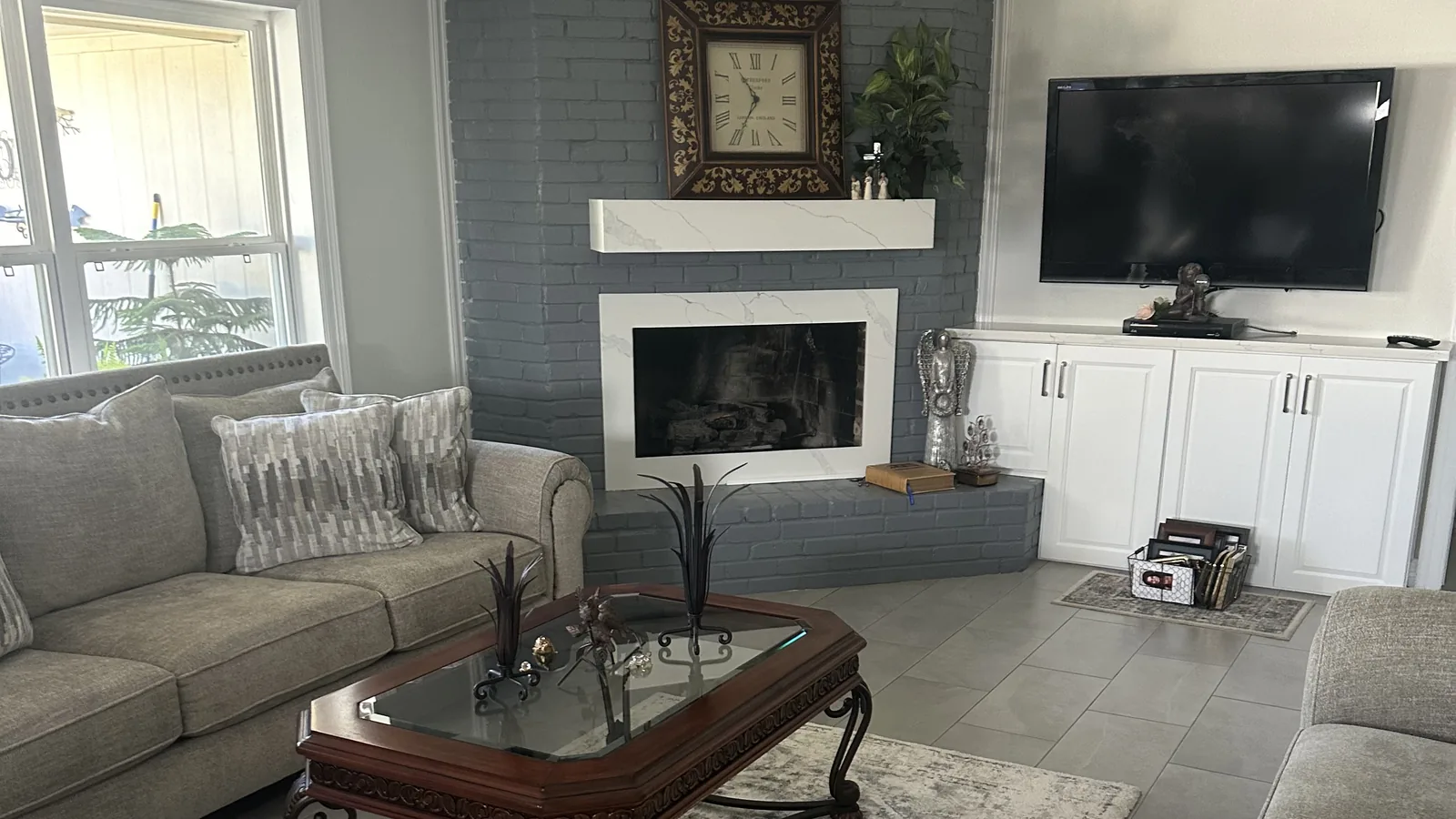 Living room with large-format gray floor tile, a painted brick fireplace and white built-in cabinets.
