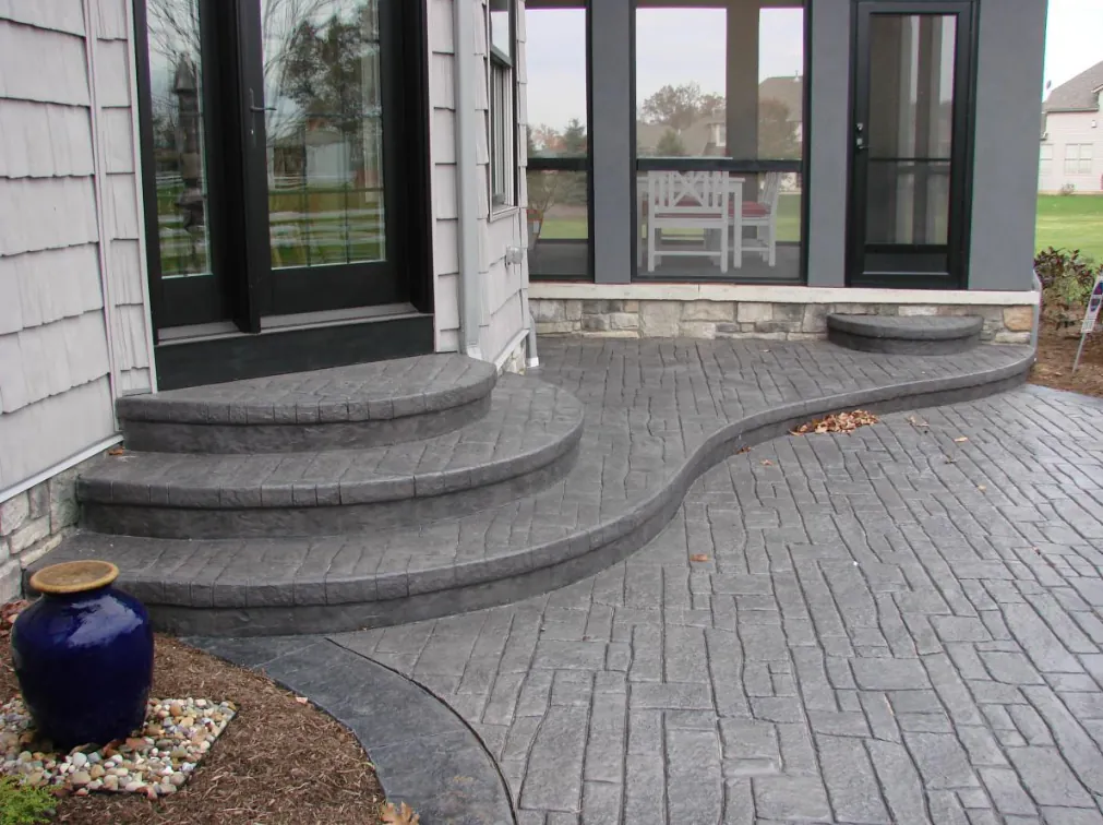 Gray stamped concrete patio with curved steps leading up to a home's glass doors.