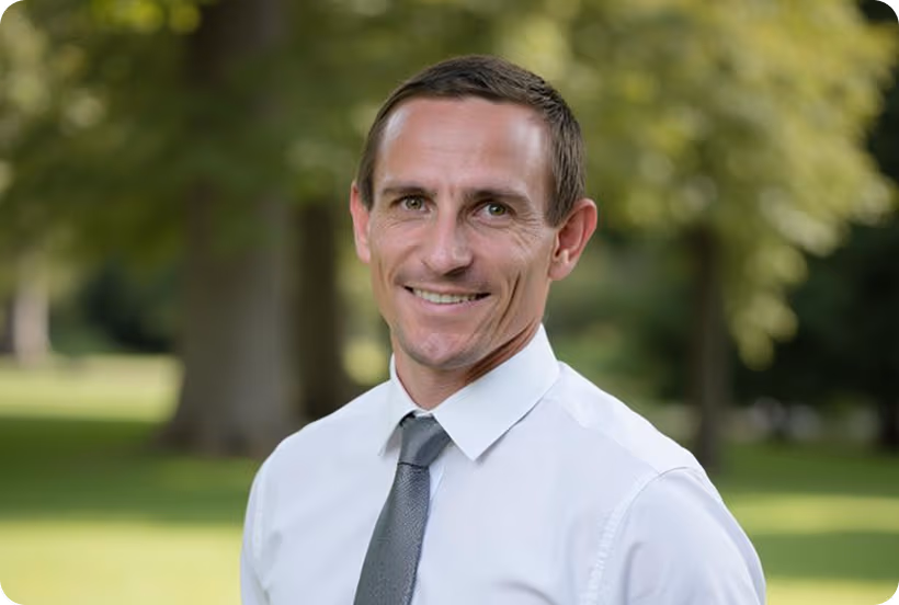 Portrait d'un homme souriant en chemise blanche et cravate gris dans un parc flou en arrière-plan.
