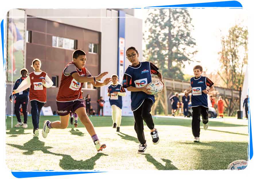 Children playing rugby on a sunny field with one player running with the ball while others chase.
