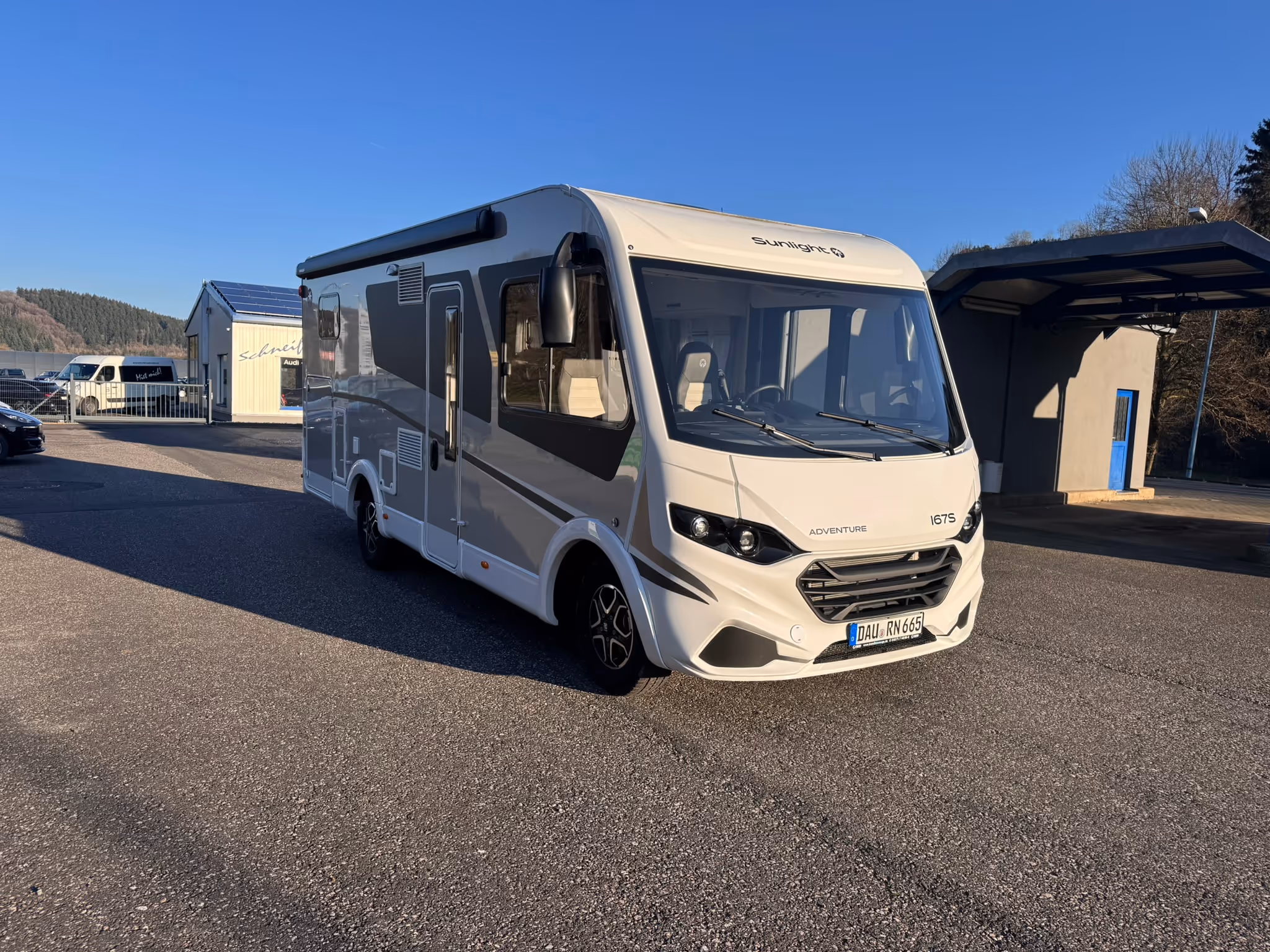 Weißes Wohnmobil der Marke Sunlight Adventure 167S auf Parkplatz bei klarem Himmel.