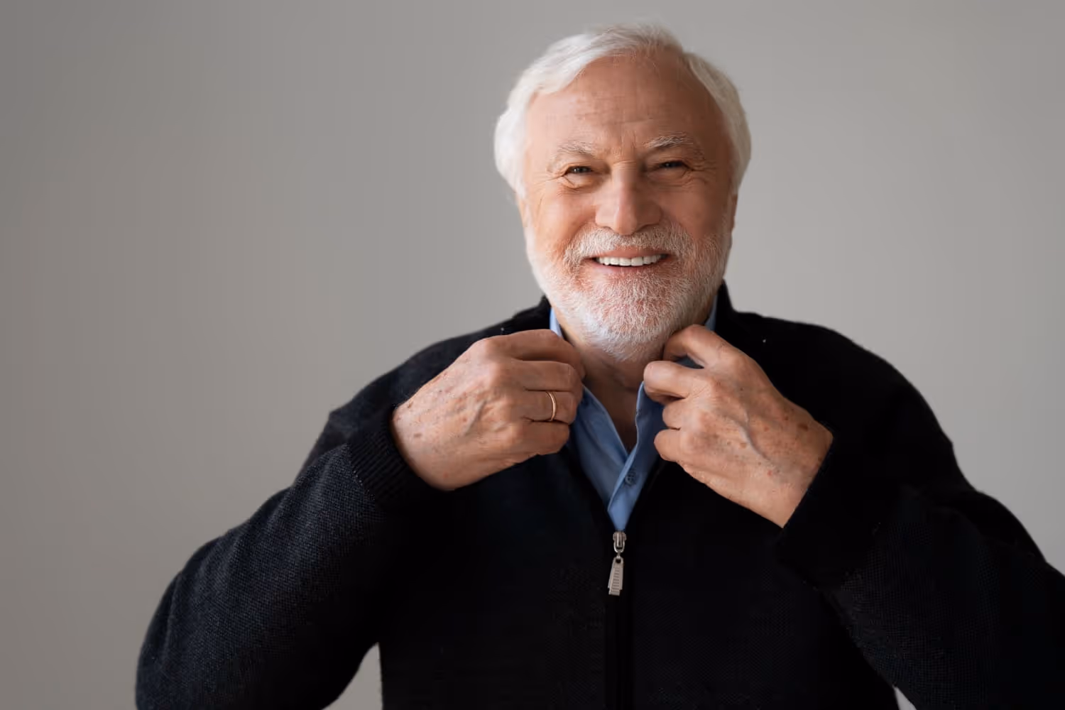 Älterer Mann mit weißem Bart und Haaren, der seine Jacke anpasst und lächelt.