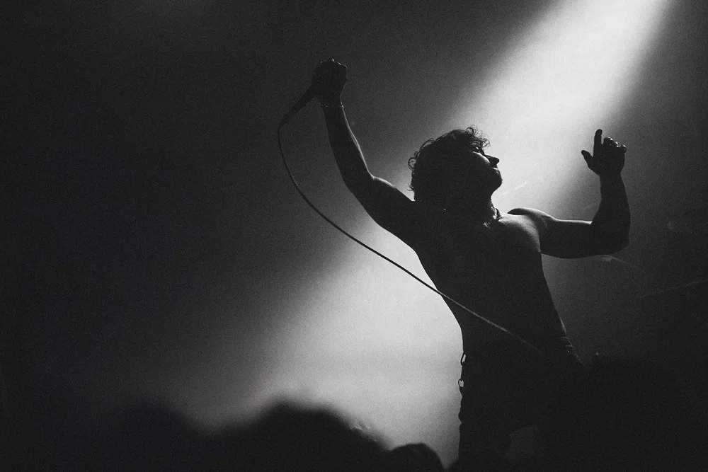 Silhouette of a shirtless male singer holding a microphone and performing under stage lights.