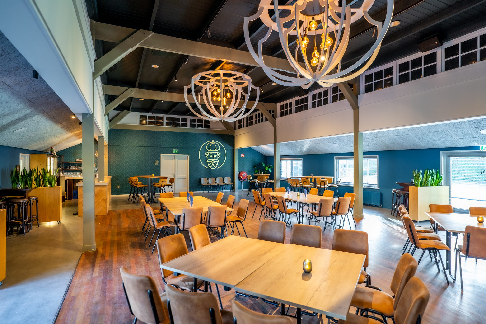 Gezellige eetzaal met houten tafels, bruine stoelen, blauwe muren en grote moderne hanglampen aan het plafond.