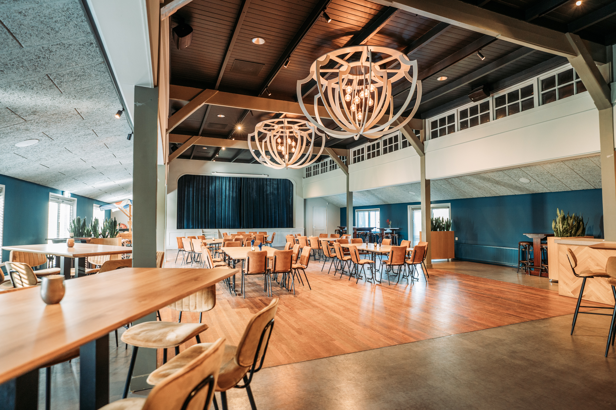 Lichte en ruime moderne zaal met houten vloeren, comfortabele stoelen en grote decoratieve hanglampen.