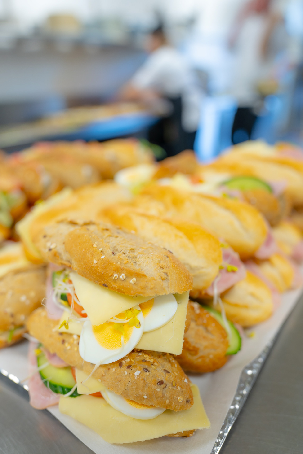 Broodjes met hardgekookte eieren, kaas, komkommer en ham op een dienblad in een keuken.