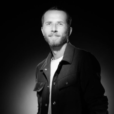 Black and white portrait of a smiling man in a white shirt and dark jacket against a plain background.