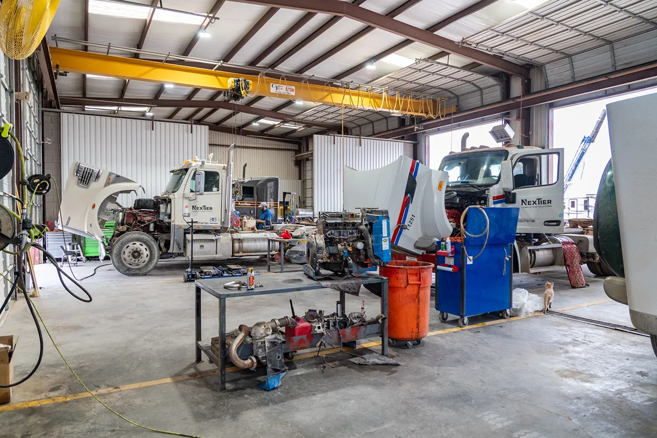 Oilfield truck repairs performed in a heavy-duty shop with multiple trucks undergoing engine and service work.