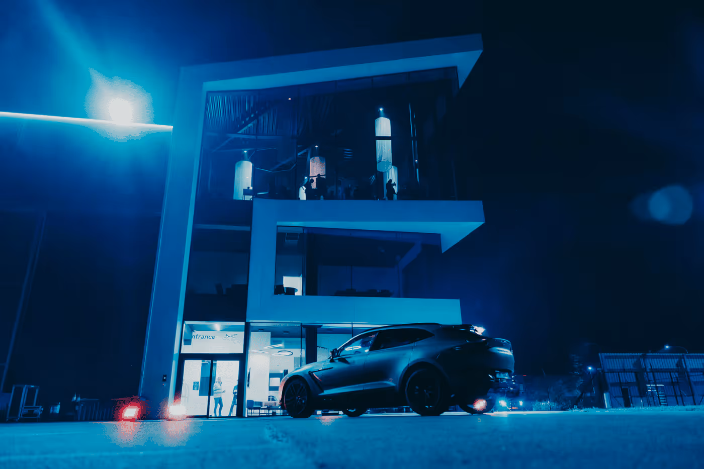 Voiture sportive noire garée devant un bâtiment moderne éclairé la nuit.