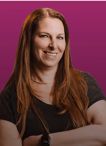 Frau mit langen braunen Haaren und schwarzem T-Shirt lächelt vor einem violetten Hintergrund.