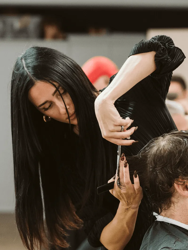 Friseurin mit langen schwarzen Haaren schneidet konzentriert einem Kunden die Haare.