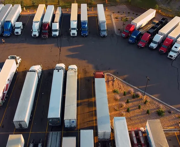 Aerial view of a parking lot with multiple parked semi-trailer trucks and trailers in organized rows.