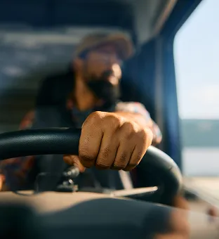 Close-up of a person's hand gripping a steering wheel while driving.