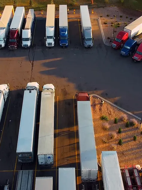 Aerial view of semi-trucks and trailers parked in a lot at sunset with long shadows.