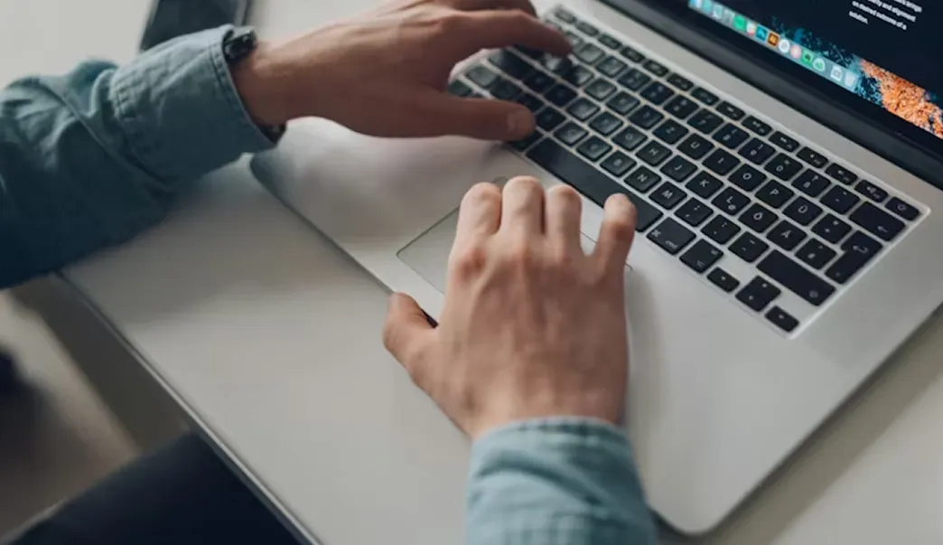 Person typing on a laptop keyboard while sitting at a desk.