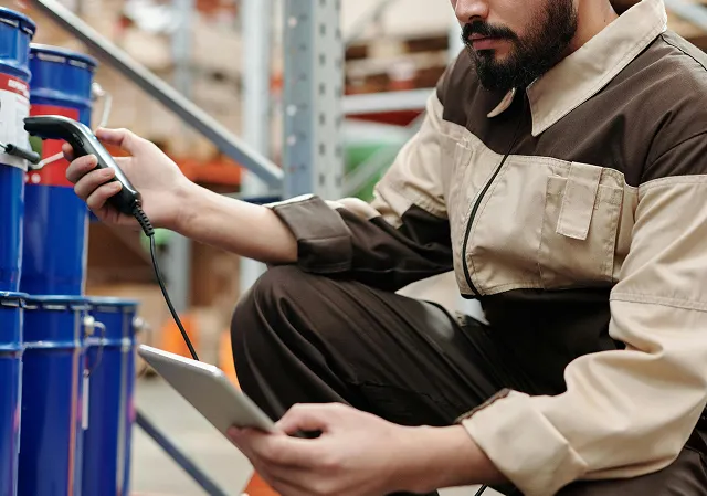 Worker in brown uniform using a barcode scanner and holding a tablet in a warehouse.