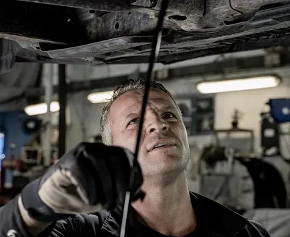 Mechanic wearing gloves inspecting underneath a vehicle in a garage.