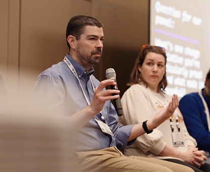 Man speaking into microphone during a panel discussion with two other panelists seated beside him.