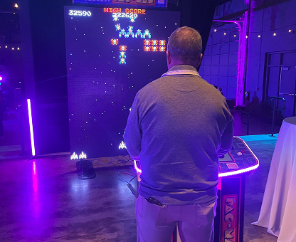 Man playing a retro arcade game with bright purple lighting in a dim room.