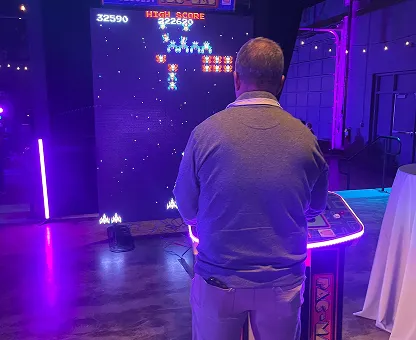 Man playing a retro arcade game with bright purple lighting in a dim room.