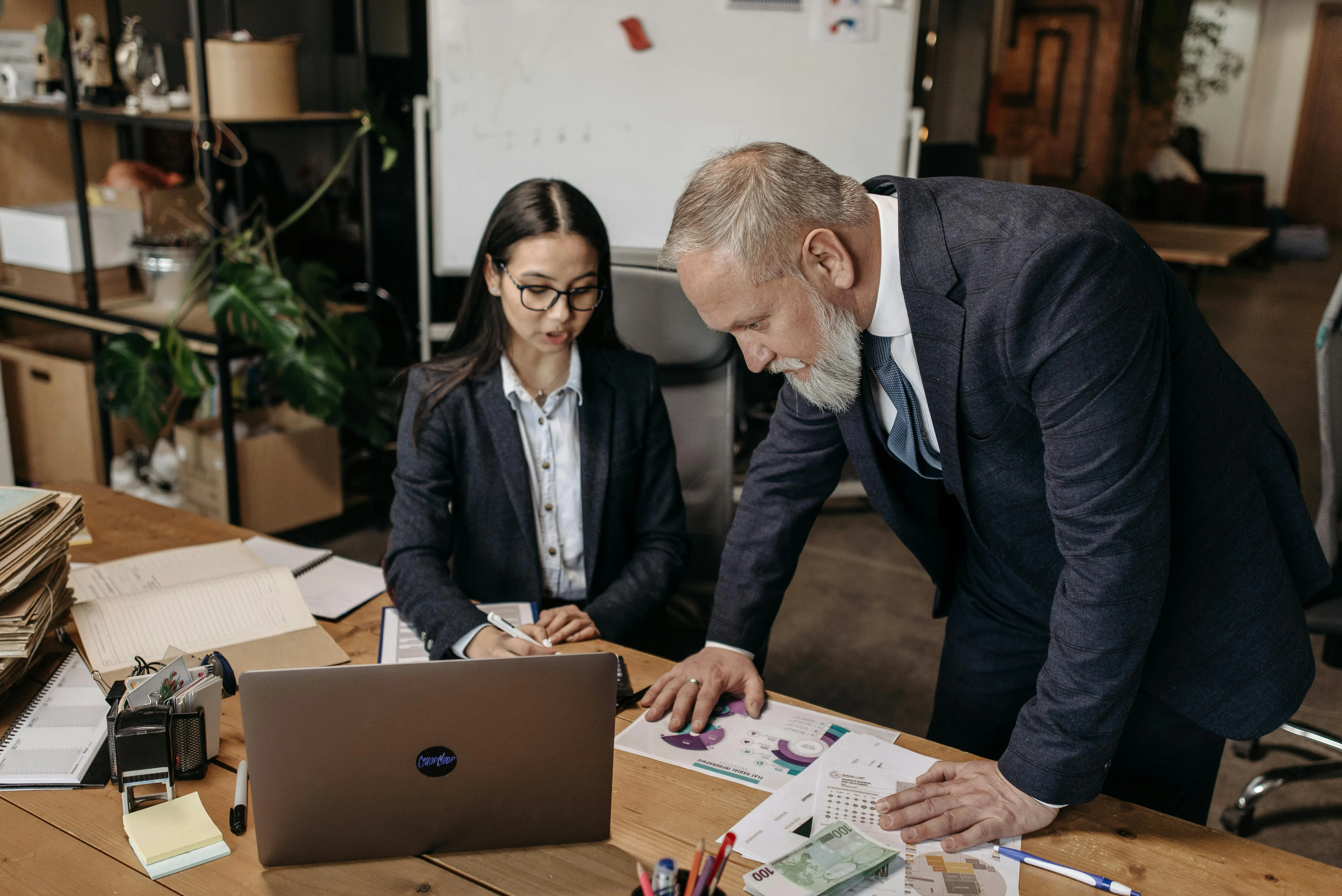 Two business professionals analyzing charts and documents together at a desk with a laptop.