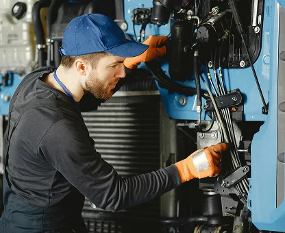 Mechanic in a blue cap and orange gloves inspecting and repairing machinery.