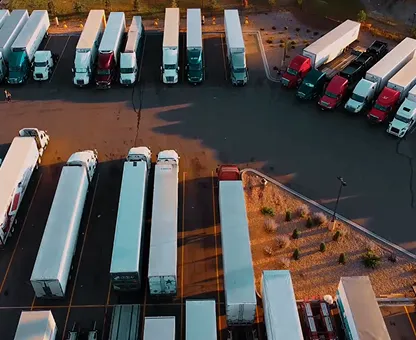 Aerial view of parked semi-trailers and trucks arranged in rows in a lot during sunset.