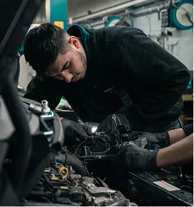 Mechanic in black hoodie working on a car engine in a garage.