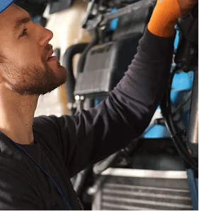 Man wearing orange gloves inspecting or repairing a vehicle engine.