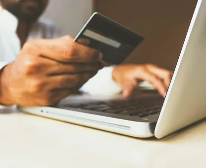 Person holding a credit card and typing on a laptop keyboard.