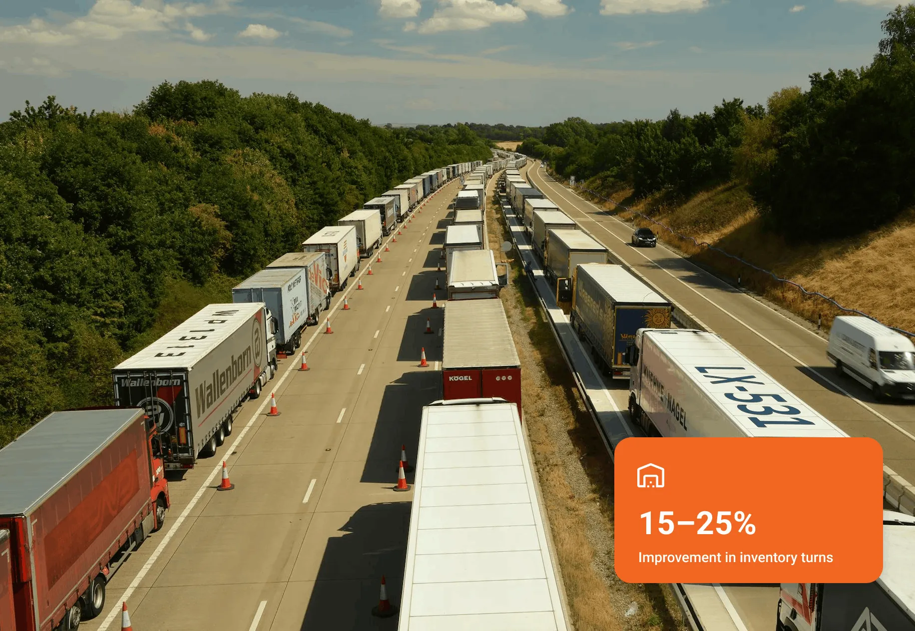 Two highway lanes filled with long lines of parked trucks and trailers separated by traffic cones, with dense green trees on either side.