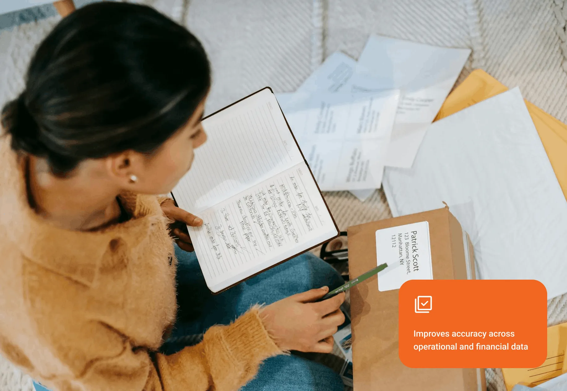 Person in a brown sweater reviewing handwritten notes and a package with a label on a carpeted floor.