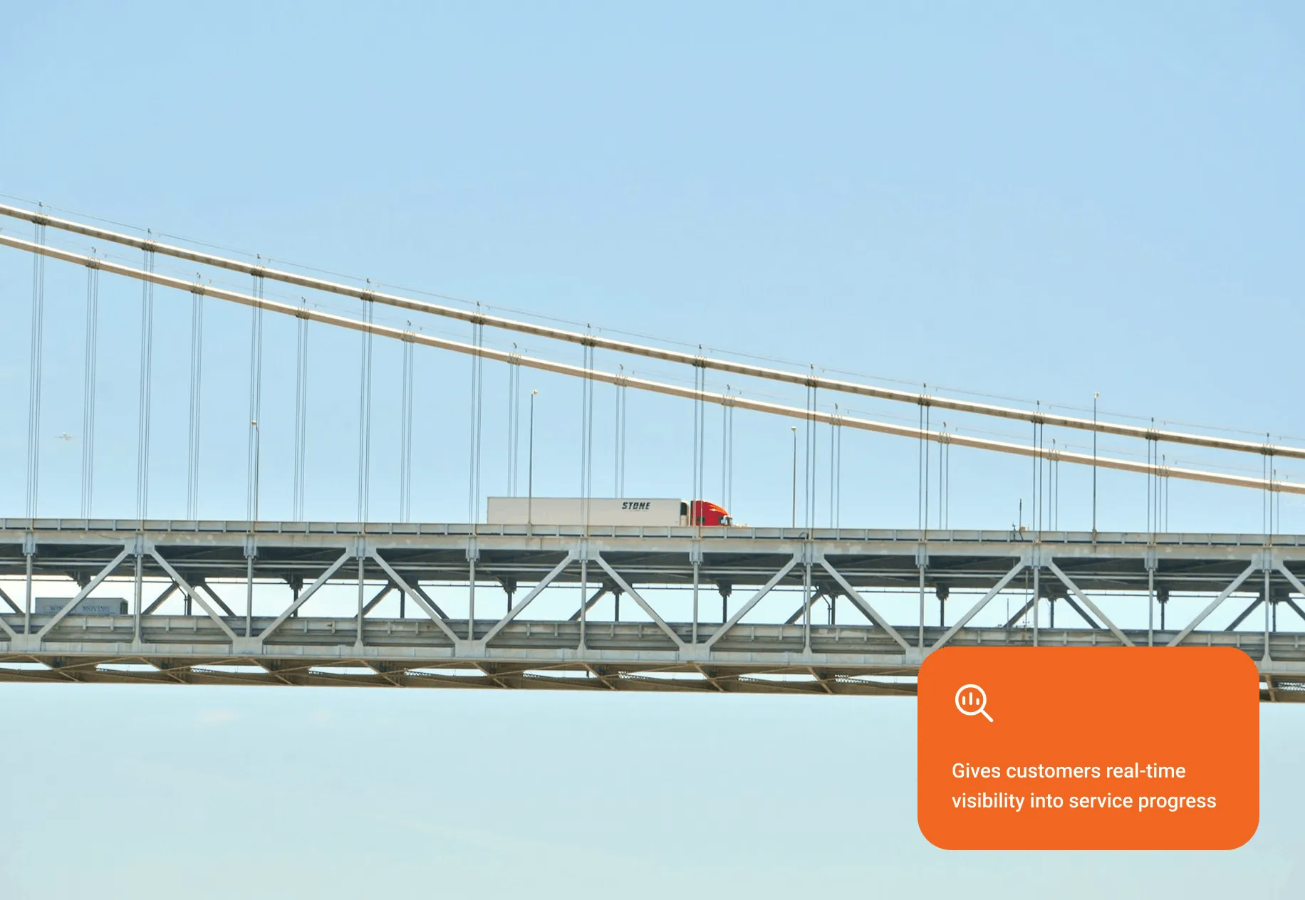 Red and white semi-truck driving on a suspension bridge under a clear blue sky.