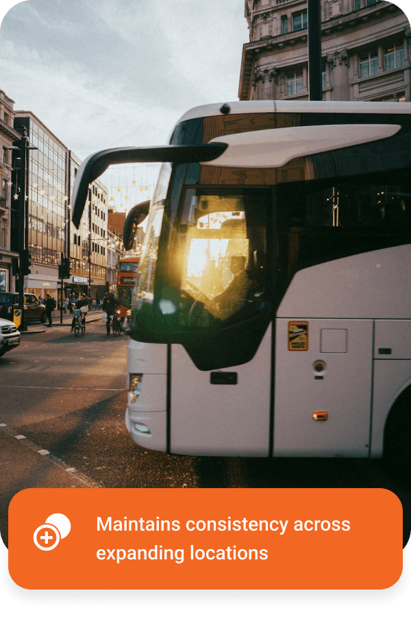 White city bus on a busy urban street with people walking and biking at sunset.