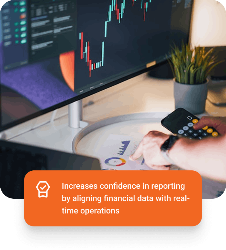 Person analyzing financial data on printed charts with calculator, next to a monitor displaying a stock market graph.