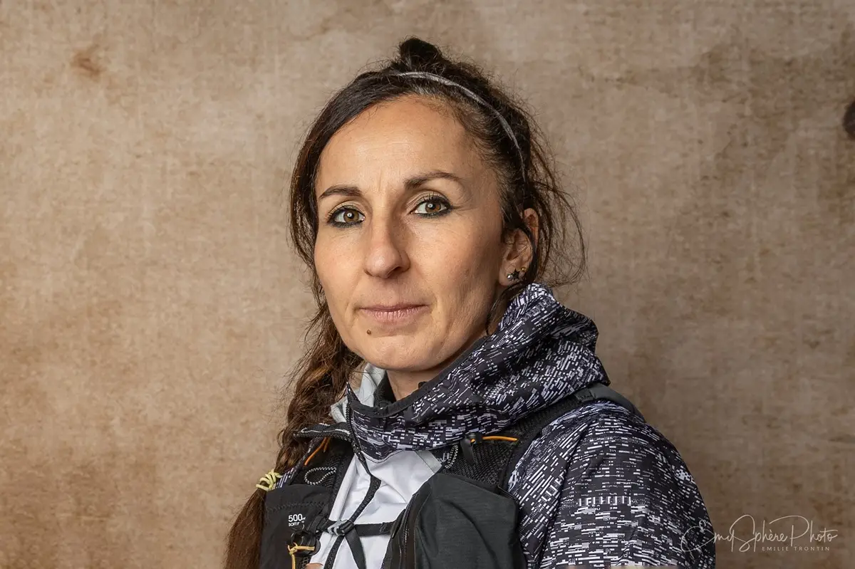 Photo pour le portrait de Maryline, marraine d'Emie. Elle pose seule devant un fond sable. Habillée en tenue de sport, prête pour ce défi et pour honorer Emie.