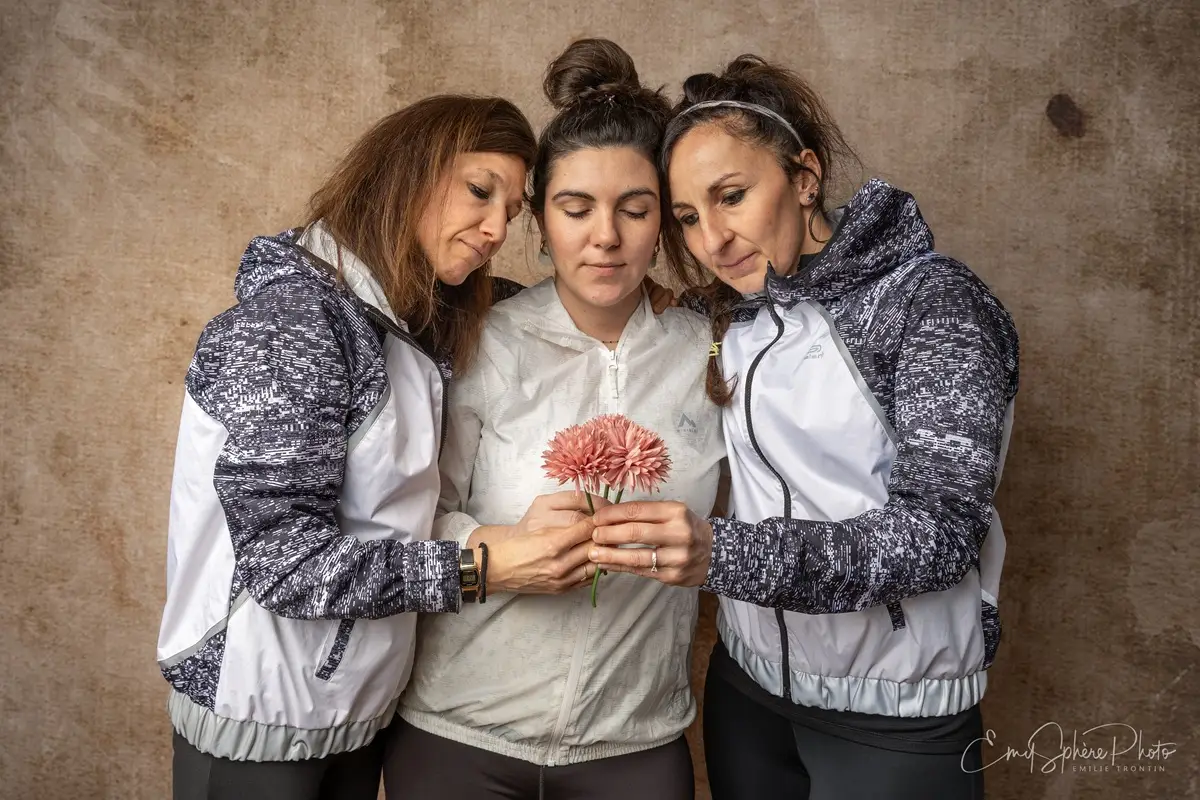 Photo pour la présentation du trio féminin. Aurelia, Laura et Maryline. Ensemble, unies, elles tiennent chacune une fleur à la main, formant à trois un bouquet en hommage à Emie.