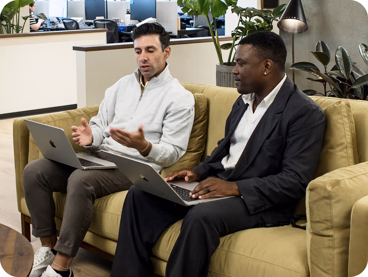 Two men sitting on a couch using laptops.