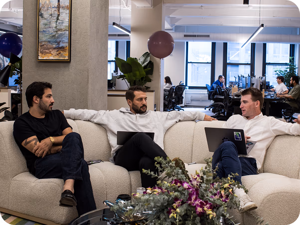 Three men sitting on a couch with laptops.