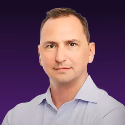 Headshot of a man with short brown hair wearing a light blue collared shirt against a dark purple background.