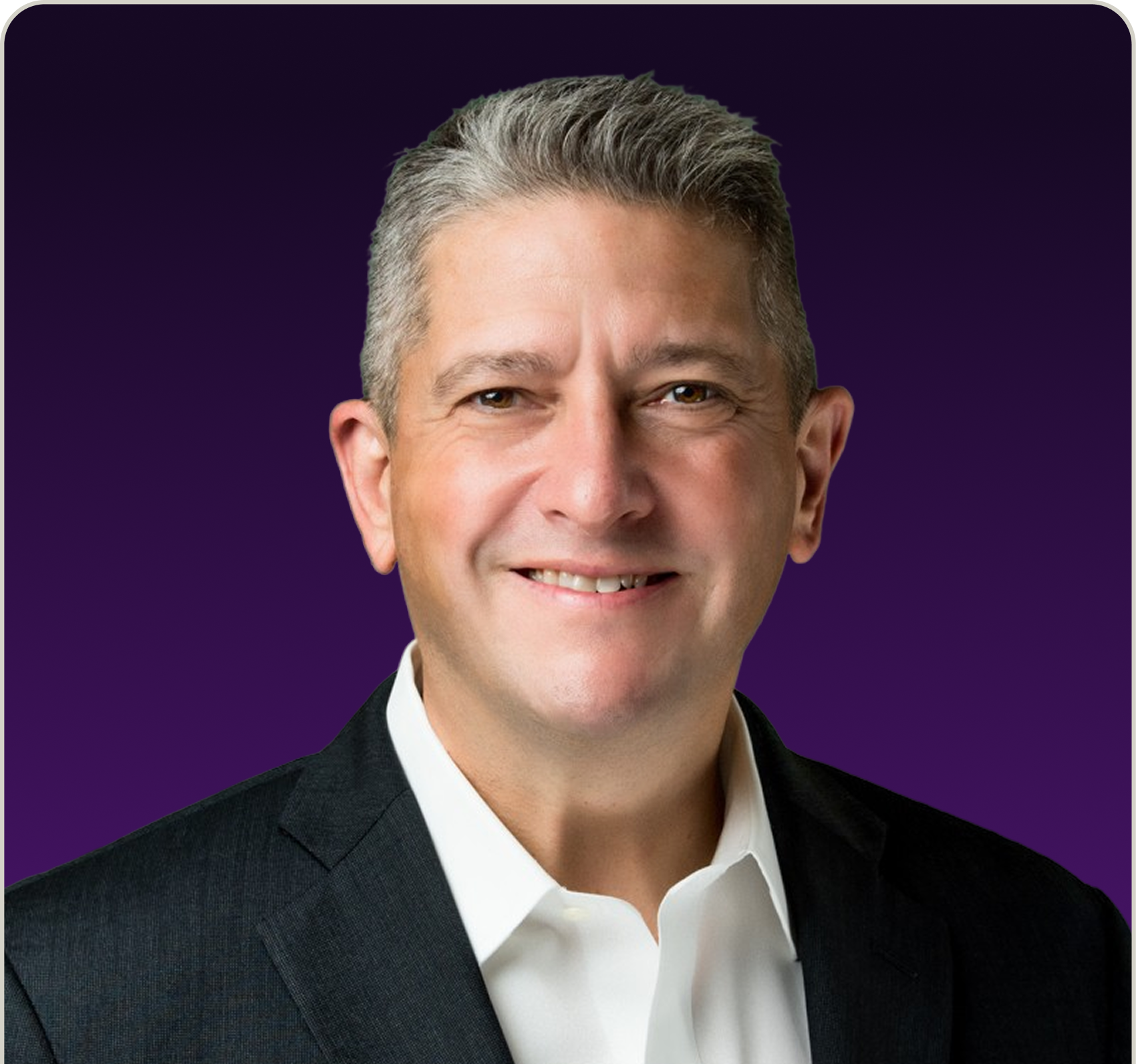 Smiling middle-aged man with short gray hair wearing a white dress shirt and dark blazer, against a purple background.