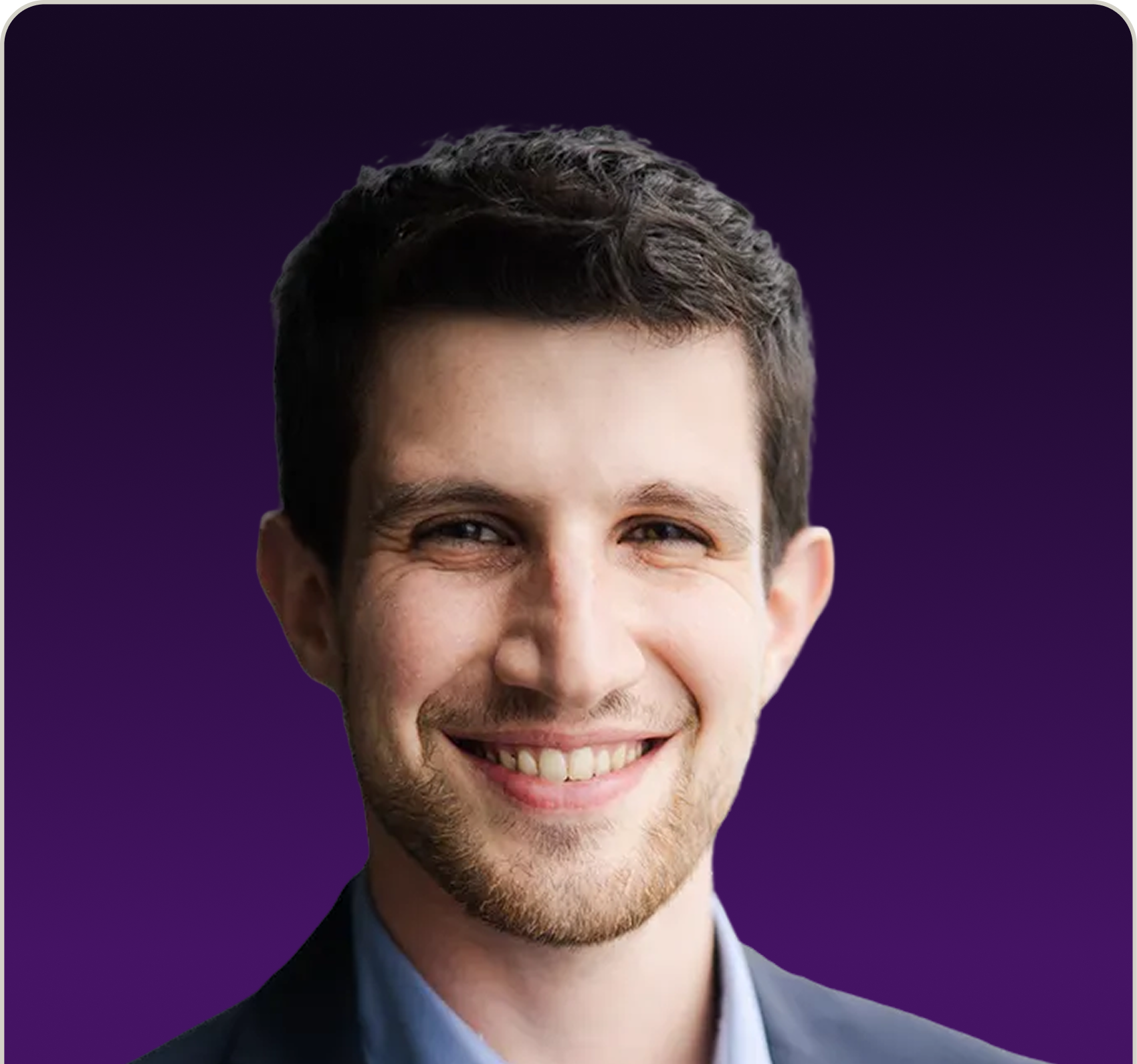 Young man with short dark hair and beard smiling against a purple background, wearing a blue collared shirt and dark jacket.