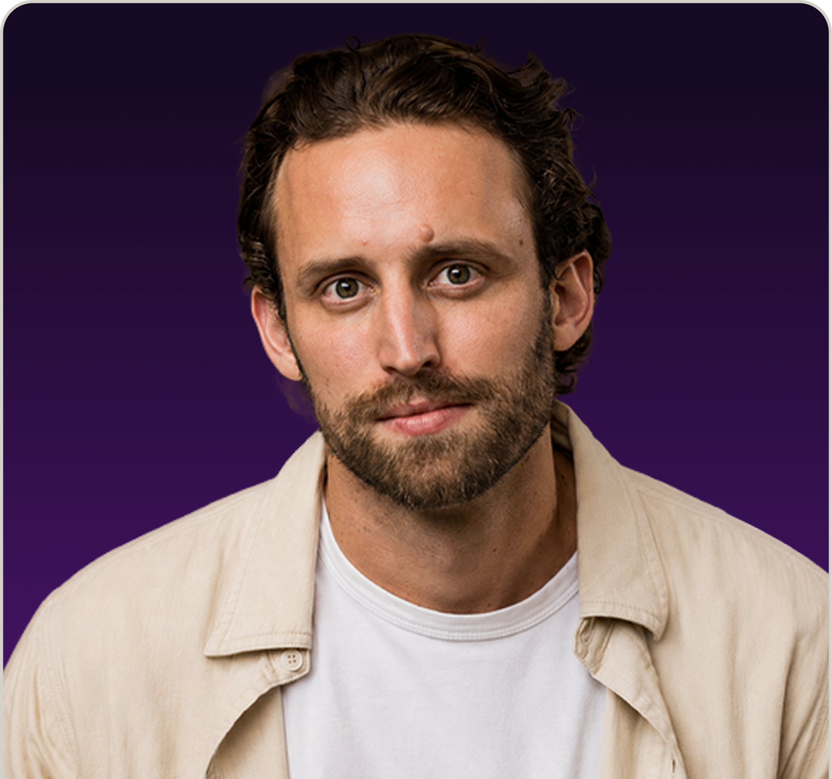 Portrait of a man with curly brown hair, stubble beard, wearing a beige jacket over a white shirt with a dark purple gradient background.