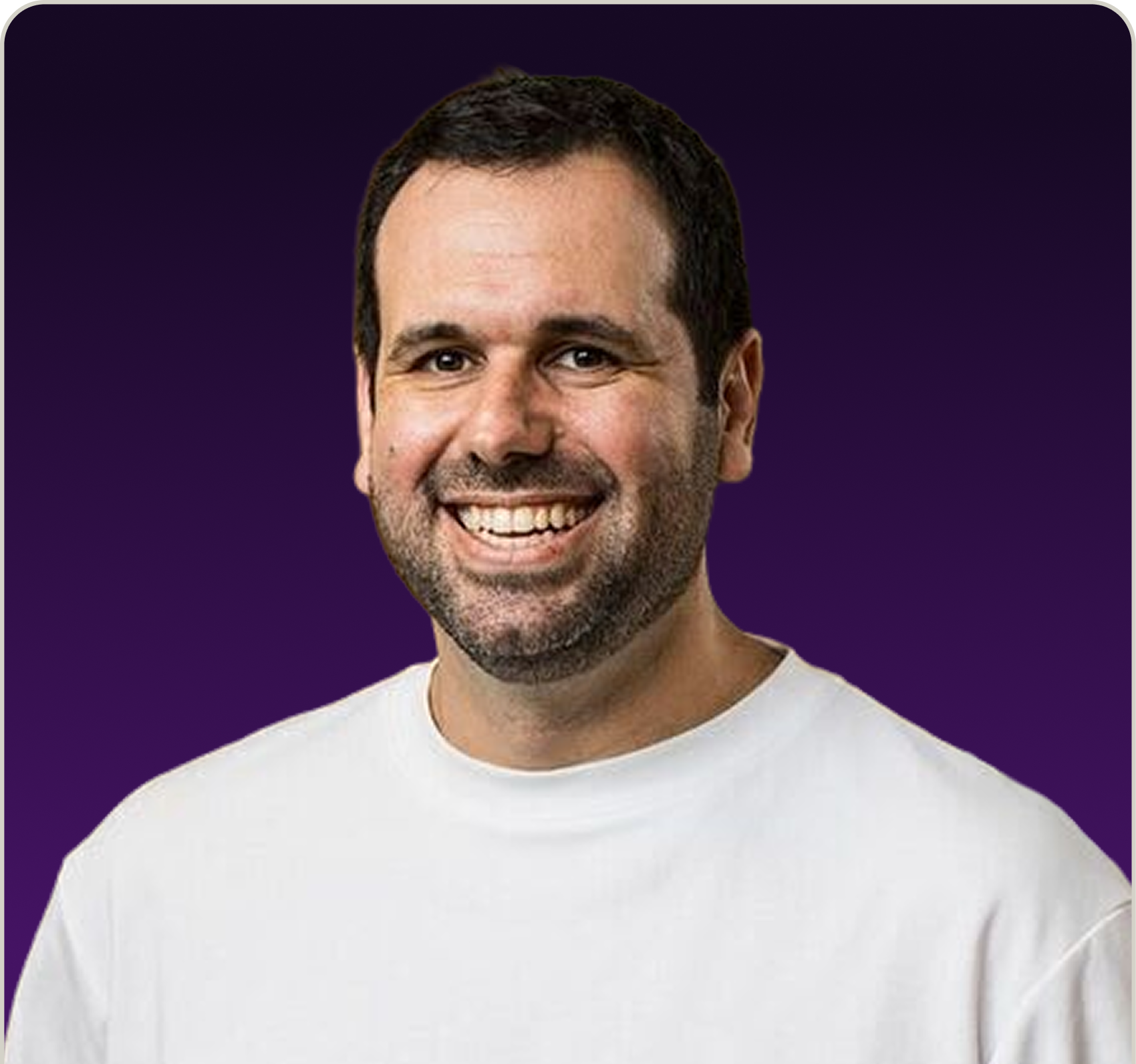 Smiling man with short dark hair and beard wearing a white shirt against a dark purple background.