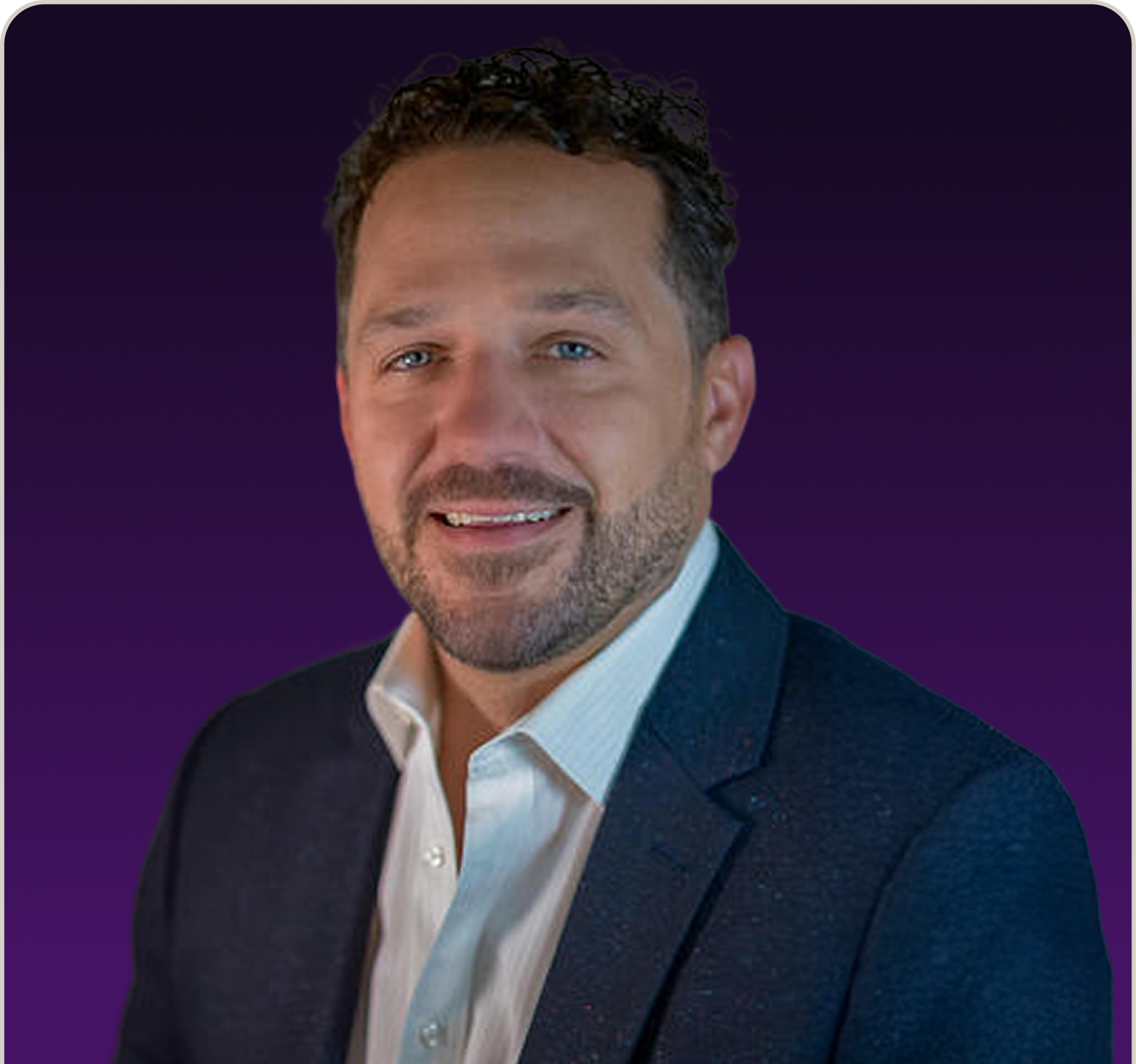 Portrait of a smiling man with curly dark hair and a beard, wearing a white dress shirt and a dark blazer against a purple gradient background.