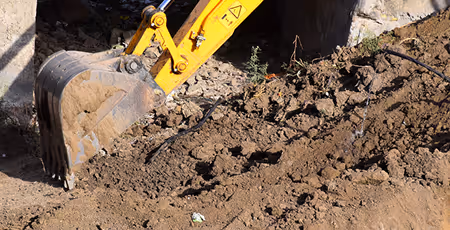 Gelber Baggerlöffel bewegt Erde auf einer Baustelle.