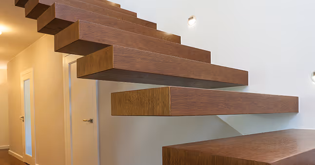 Schwebende Holztreppe mit klaren, rechteckigen Stufen an einer weißen Wand in einem modernen Innenraum.