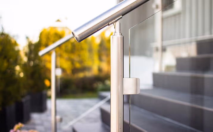 Nahaufnahme eines modernen Edelstahl-Handlaufs mit Glasgeländer neben Außentreppe.