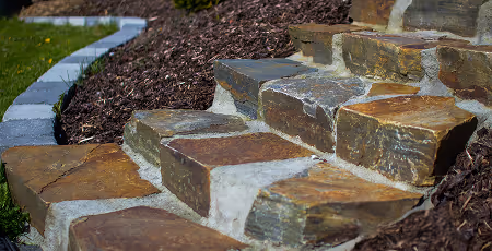 Natürliche Terrassenstufen aus Stein mit braunem Mulch rechts und Rasen links.