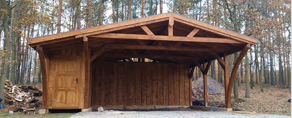 Holzcarport mit angrenzendem Abstellraum in einem Waldgebiet.